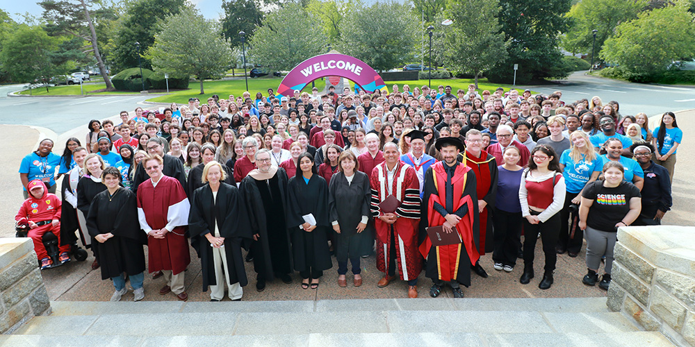 A large group of faculty, staff and students with welcome sign in the bground.